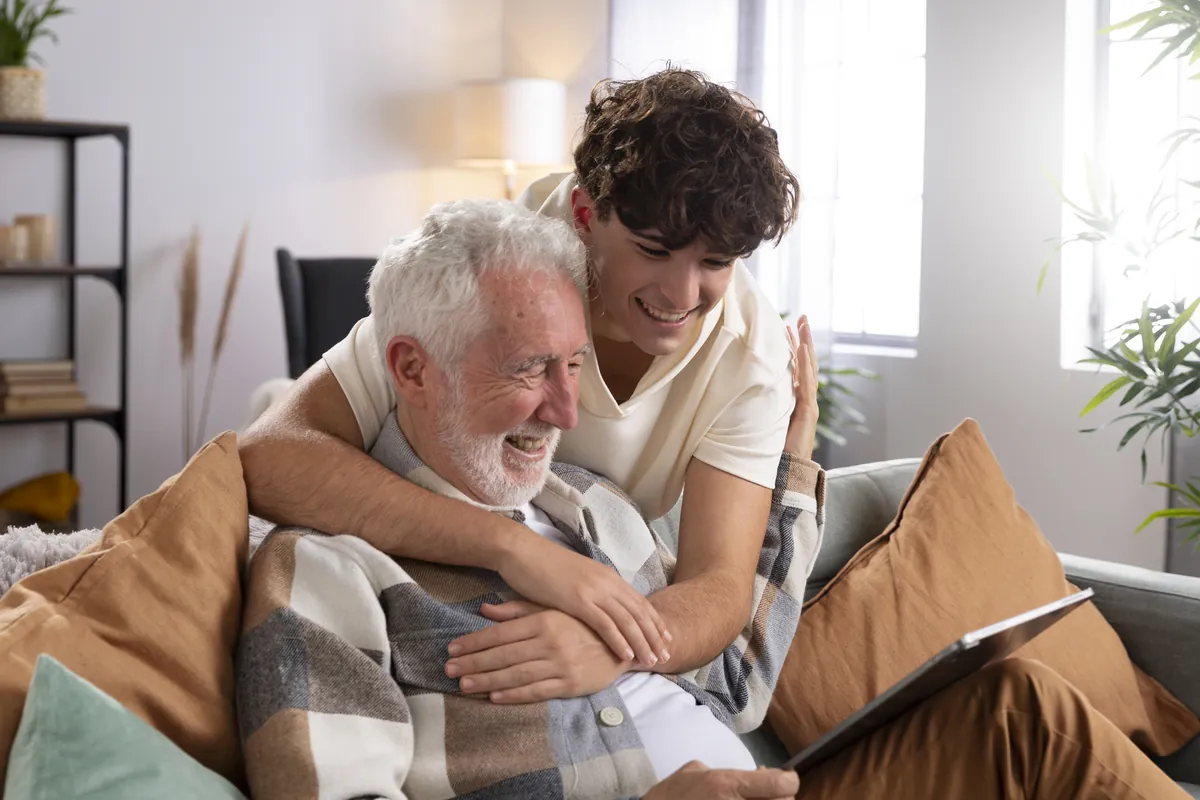 Un joven abraza a su abuelo mientras miran juntos una tablet